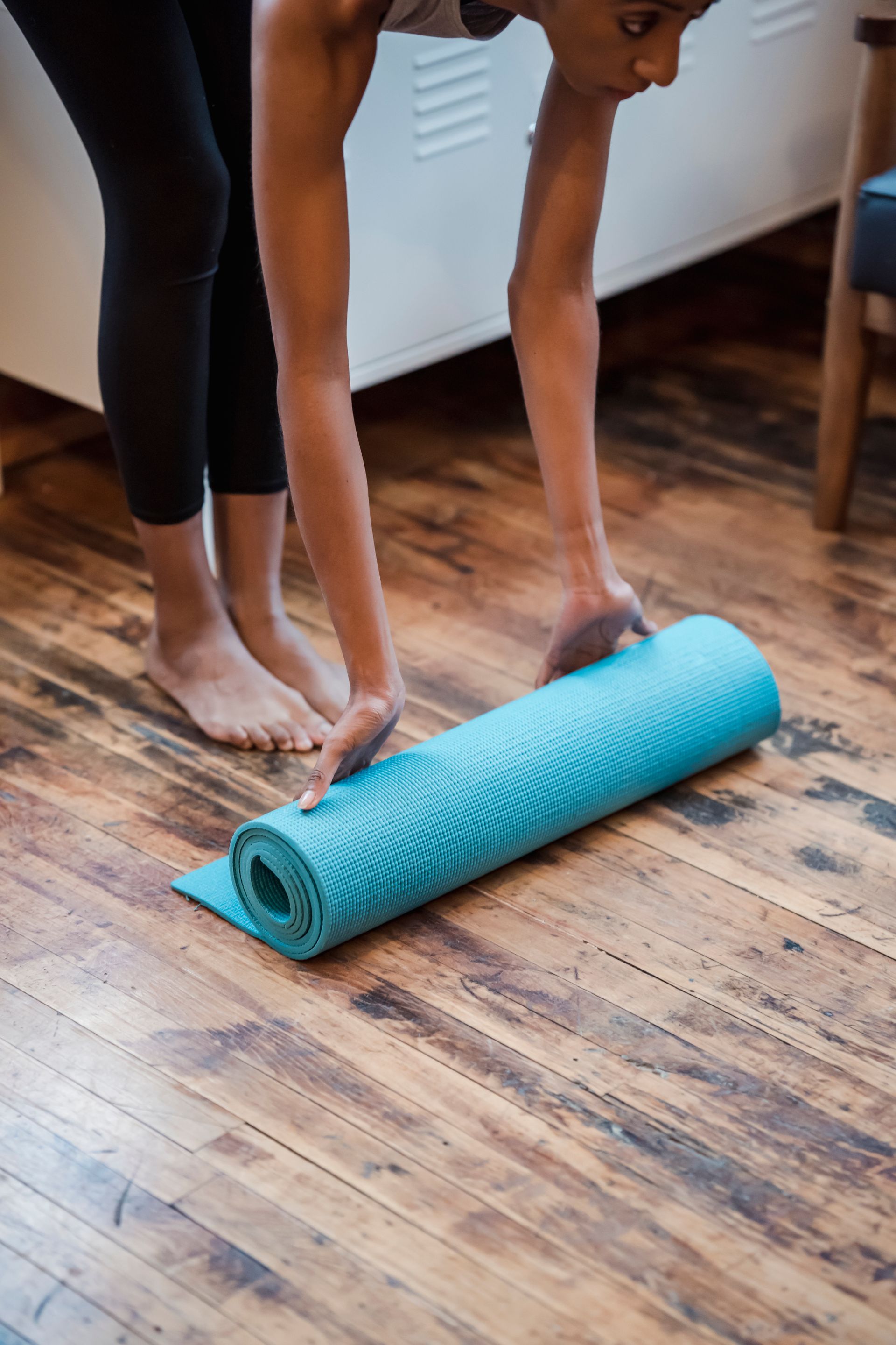black female placing yoga mat on floor in room